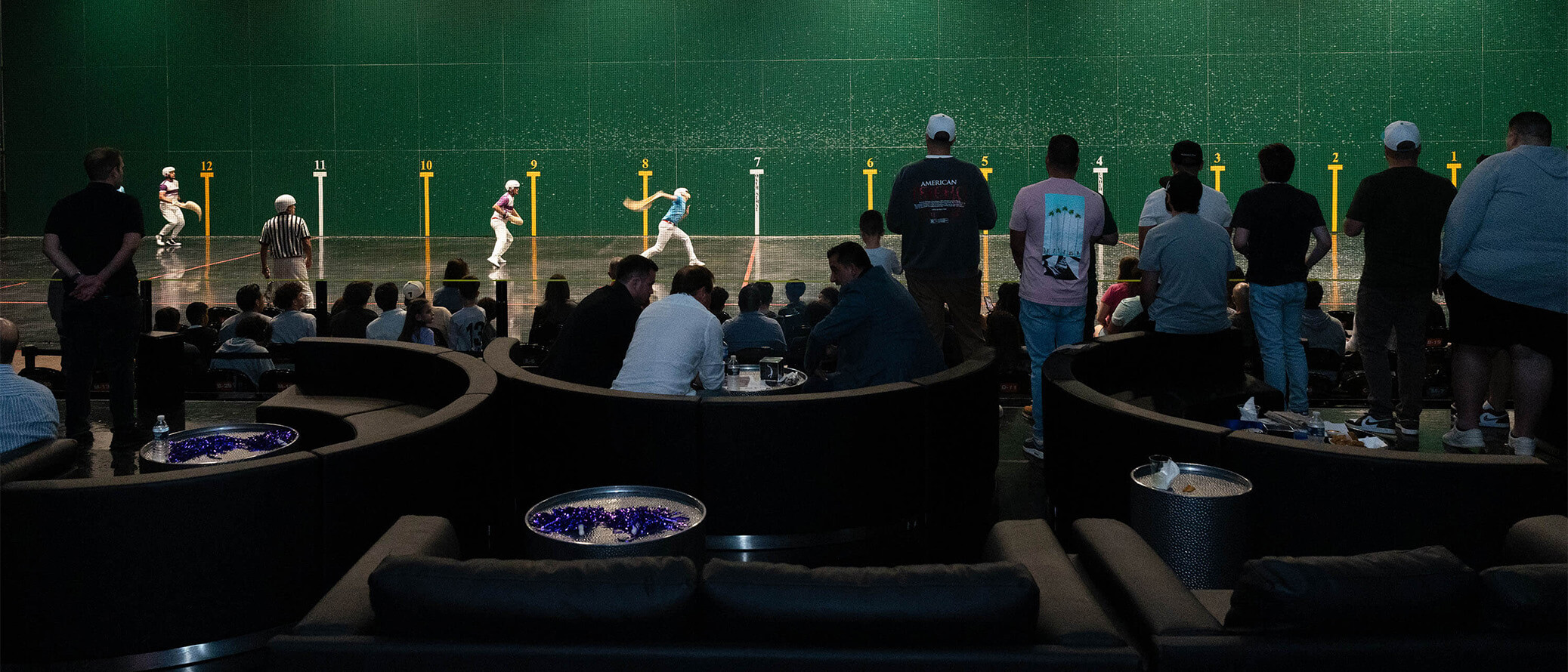 Spectators watching a Jai Alai rally from seats beside the court